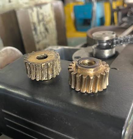Dos engranajes de bronce: uno desgastado y uno recién fabricado, lado a lado.